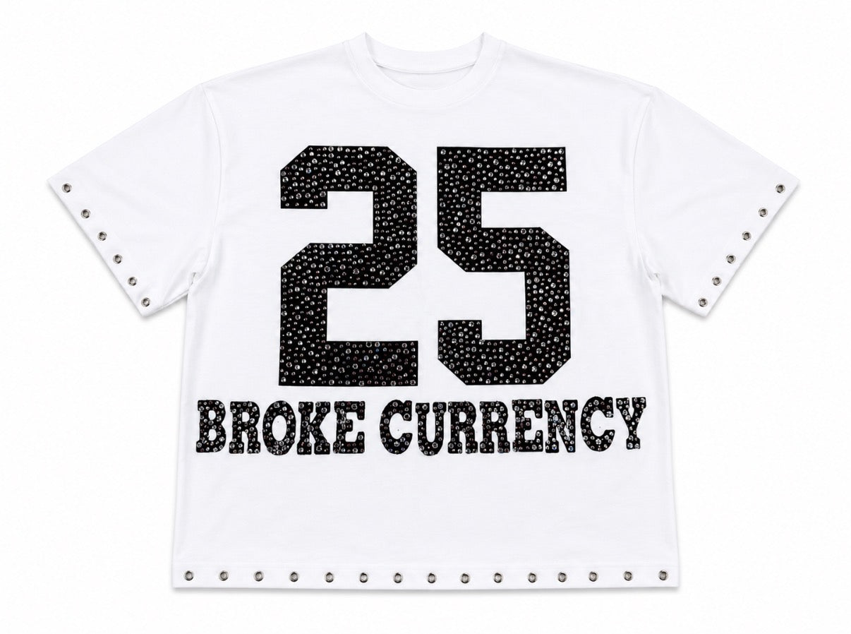 A white short-sleeve t-shirt with a black rhinestone-embellished '25' graphic and 'BROKE CURRENCY' text on the front, finished with silver-tone studs along the sleeve cuffs and hem.