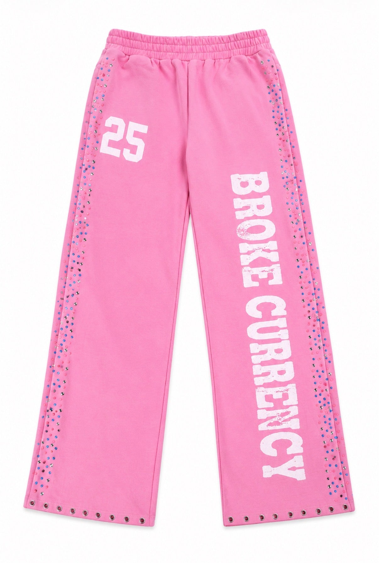 Pink sweatpants with 'BROKE CURRENCY' printed vertically in white on one leg, the number '25' on the other leg, and multicolored studs along the side seams and hem.