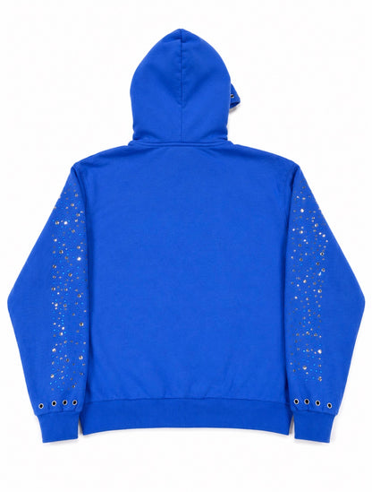 A bright blue zip-up hoodie shown from the back, featuring decorative silver rhinestone embellishments running down both sleeves and silver grommets near the cuffs.